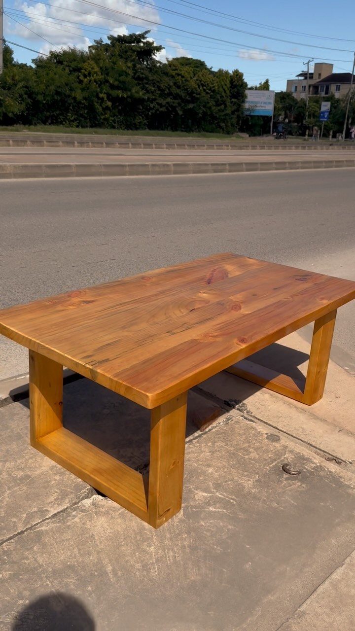 Wooden coffee table with a natural finish on a concrete sidewalk outdoors.