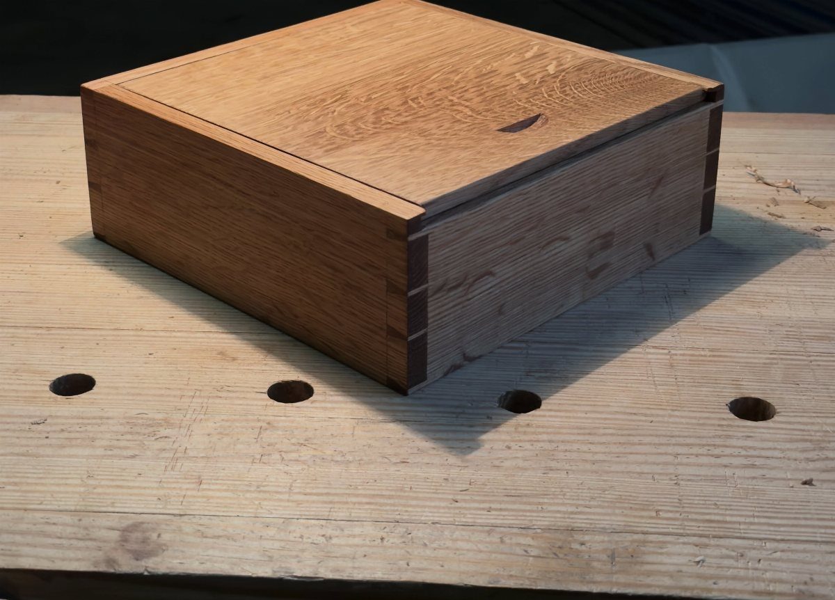 Wooden keepsake box with a lid sitting on a light wood workbench.