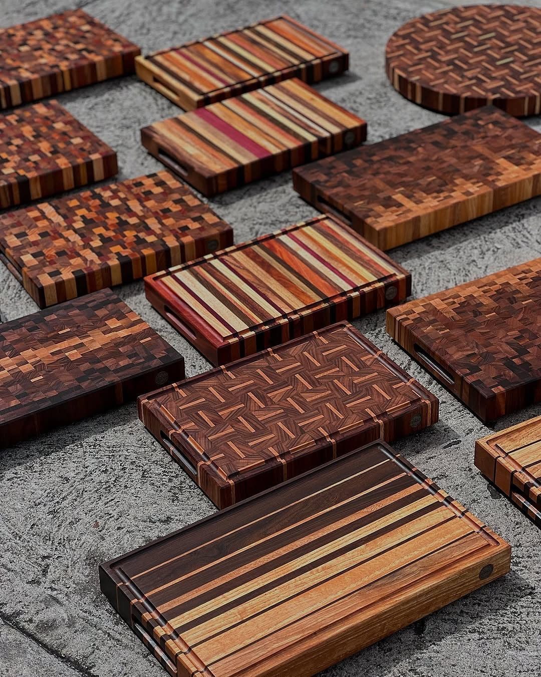 Various wooden cutting boards with striped and mosaic patterns on a grey surface.
