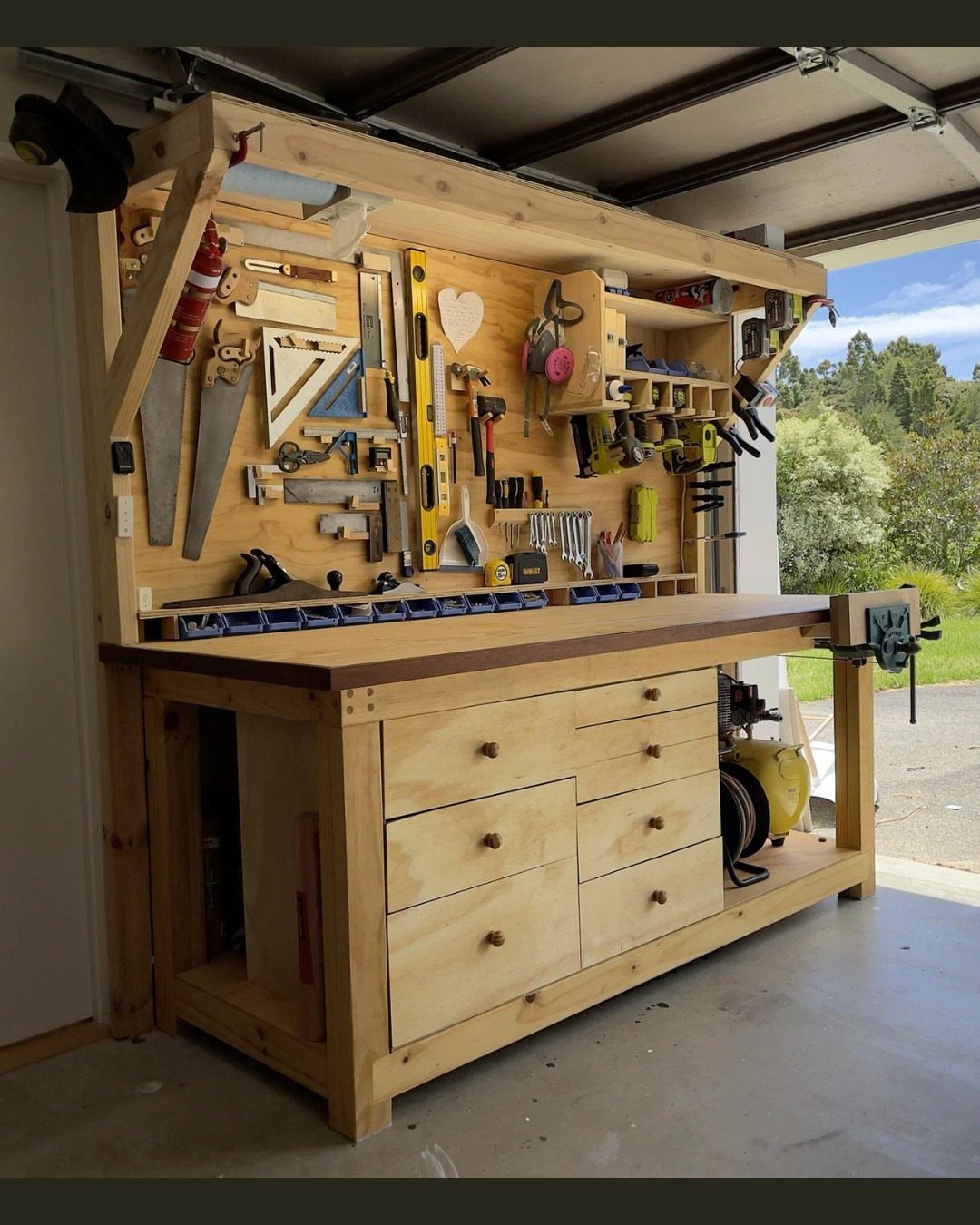 Wooden shop workbench with a tool-organized backboard and drawers in a garage setting.