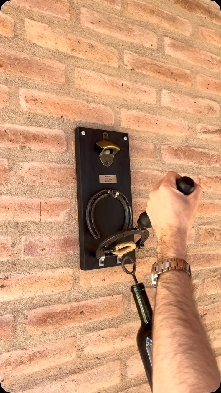 Wall-mounted bottle opener on a black wooden board attached to a brick wall.