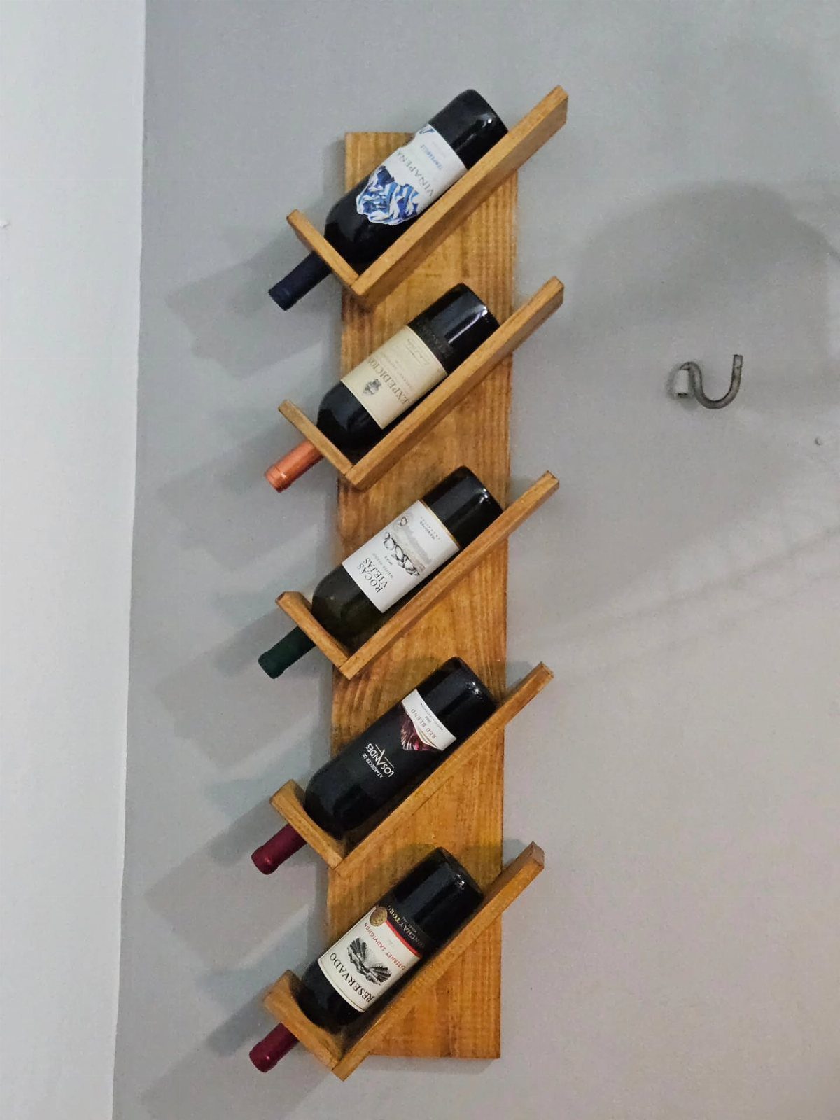 Wooden wall-mounted wine rack holding five bottles of wine in diagonal slots.