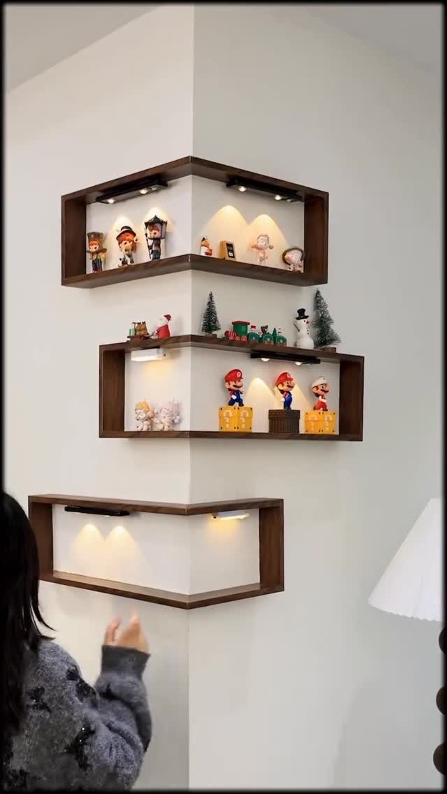 Dark brown wooden corner shelves with integrated lighting displaying small figurines on white walls.