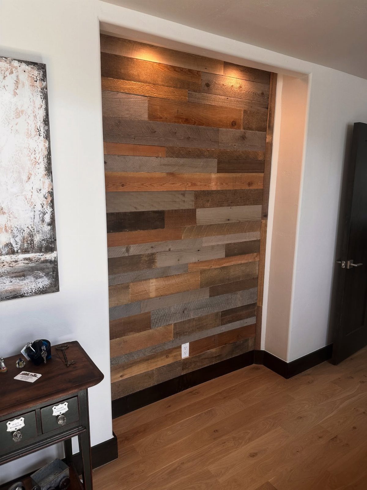 Reclaimed wooden plank accent wall in a room with white walls and hardwood flooring.