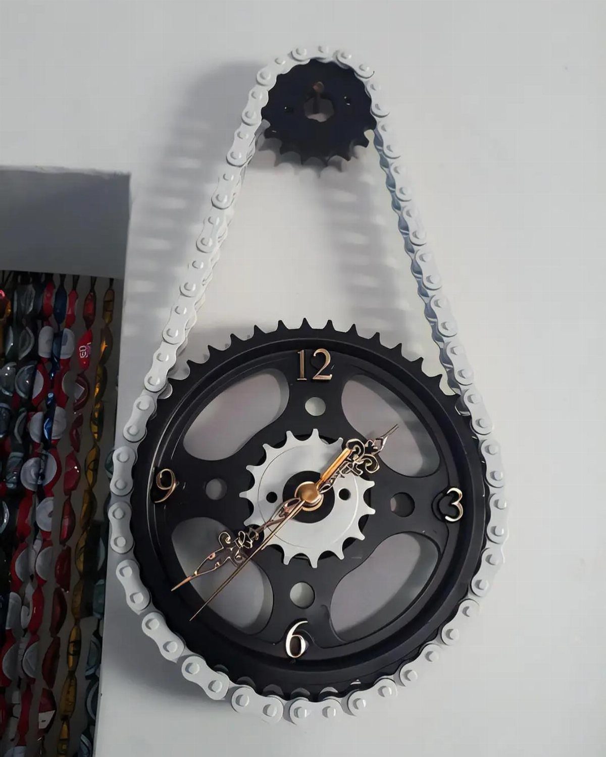 Metal gear clock with a white chain mounted on a white wall