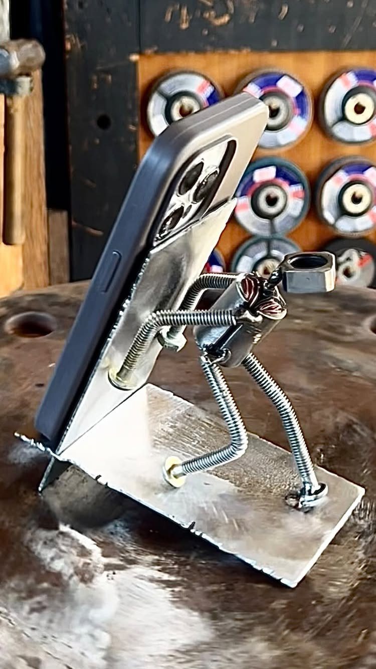 Welded metal phone stand shaped like a figure holding a grey smartphone