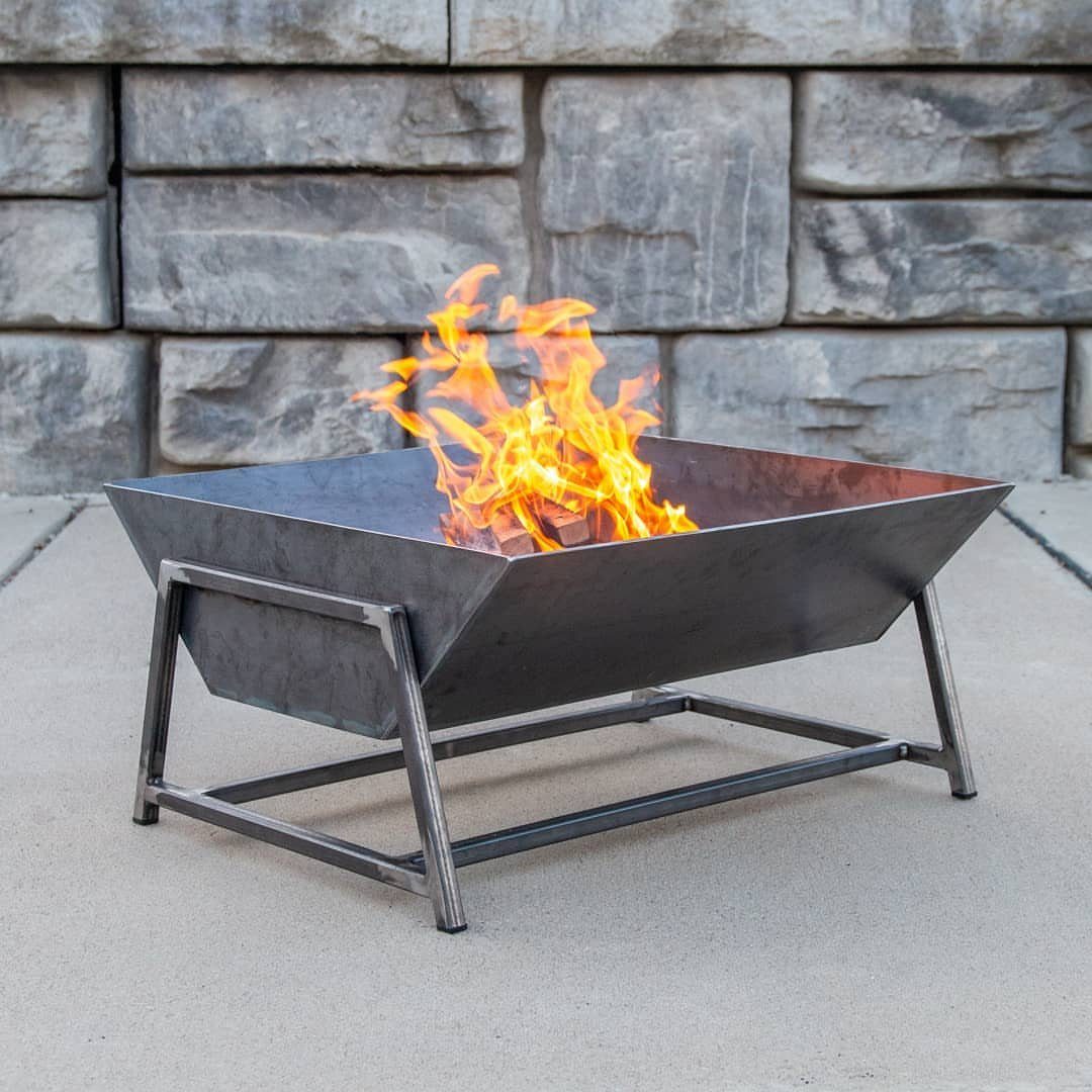 Square metal fire pit with burning orange flames on a concrete patio