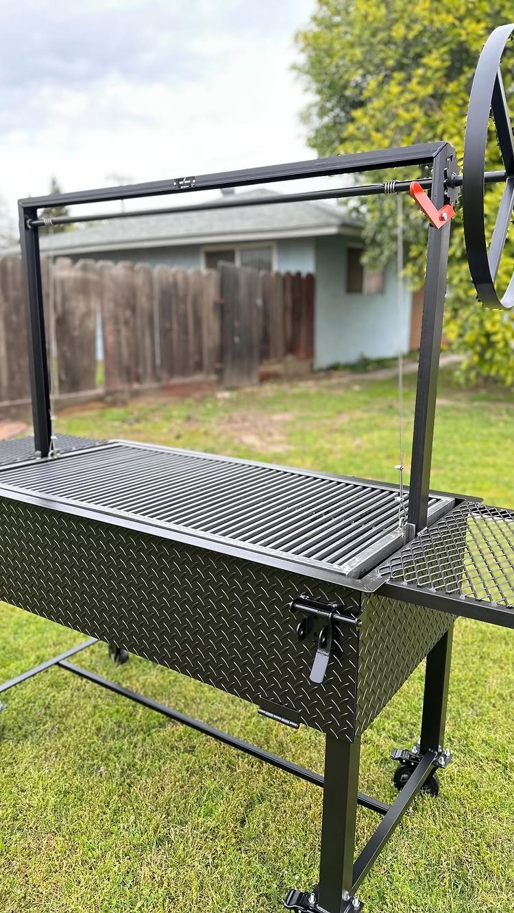 Black metal BBQ grill with rotisserie attachment on a green grassy lawn