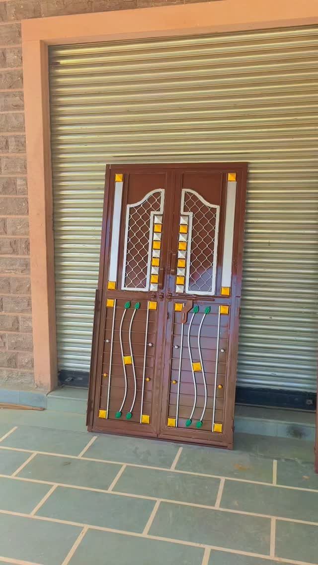 Brown metal double gate with decorative white and yellow accents leaning against a shutter.