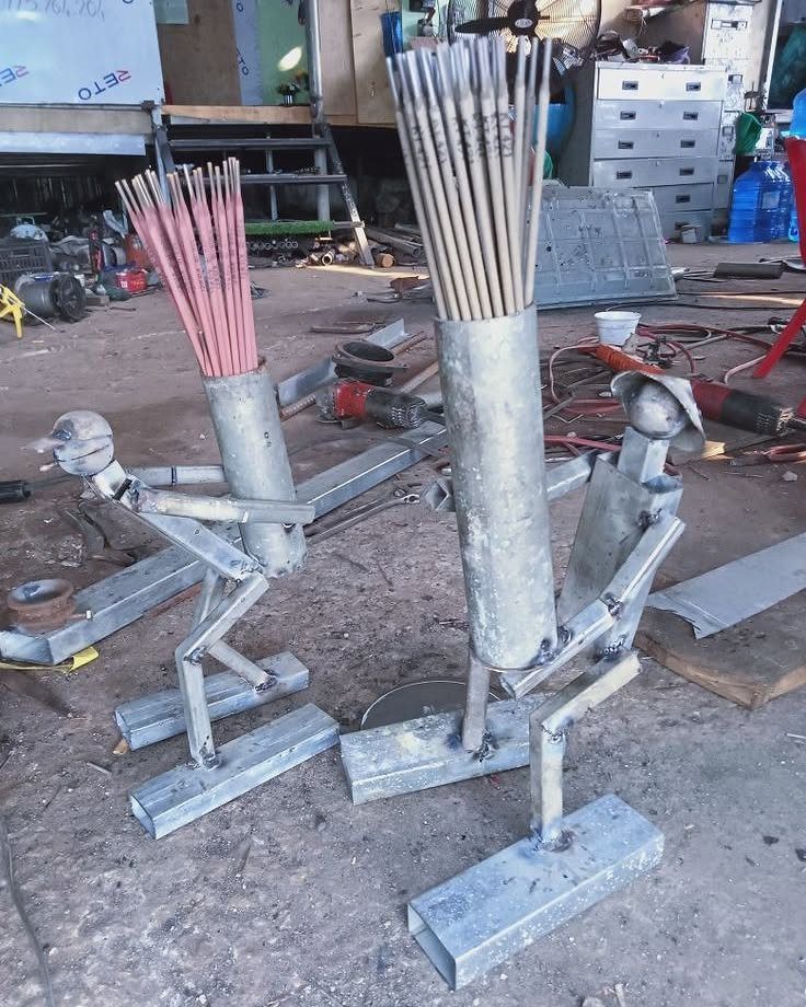 Two welded metal figures holding bundles of welding rods in a workshop