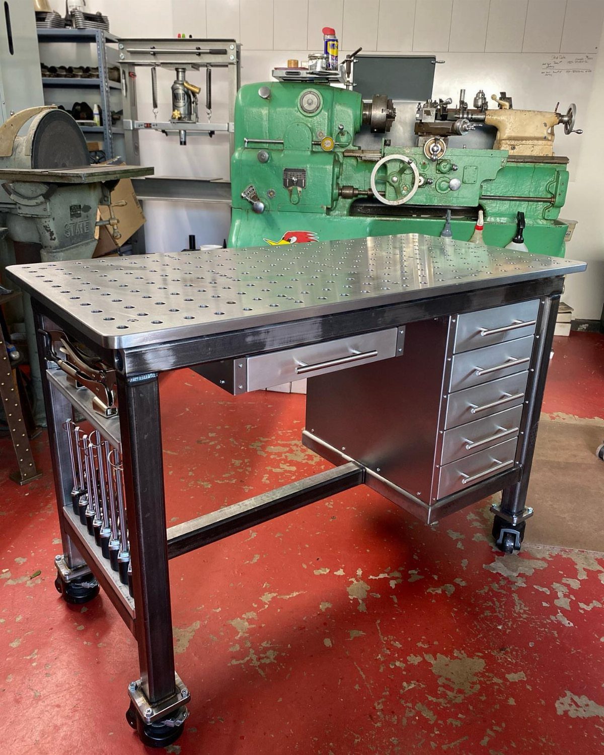 Metal welding table with perforated top and storage drawers in a machine shop.
