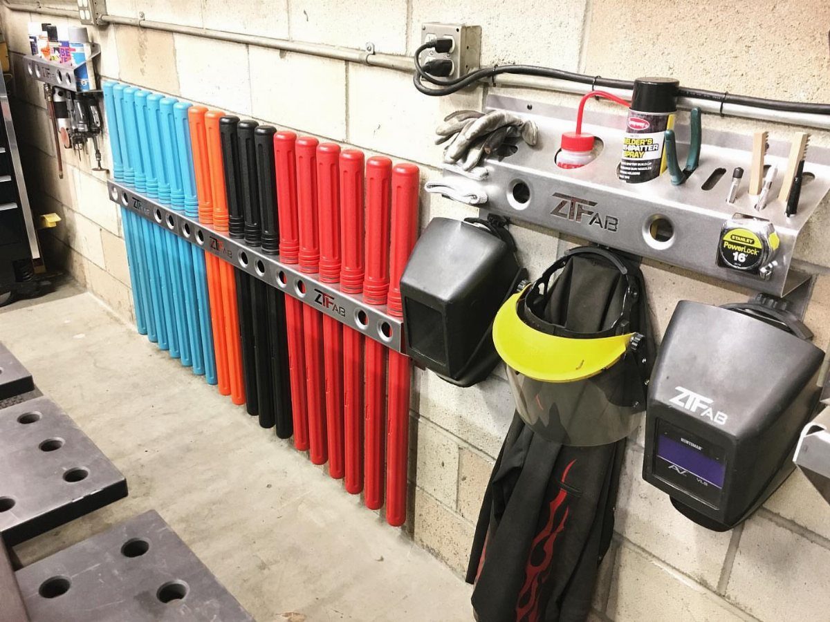 Metal tool rack holding colorful tubes and welding helmets on a white brick wall