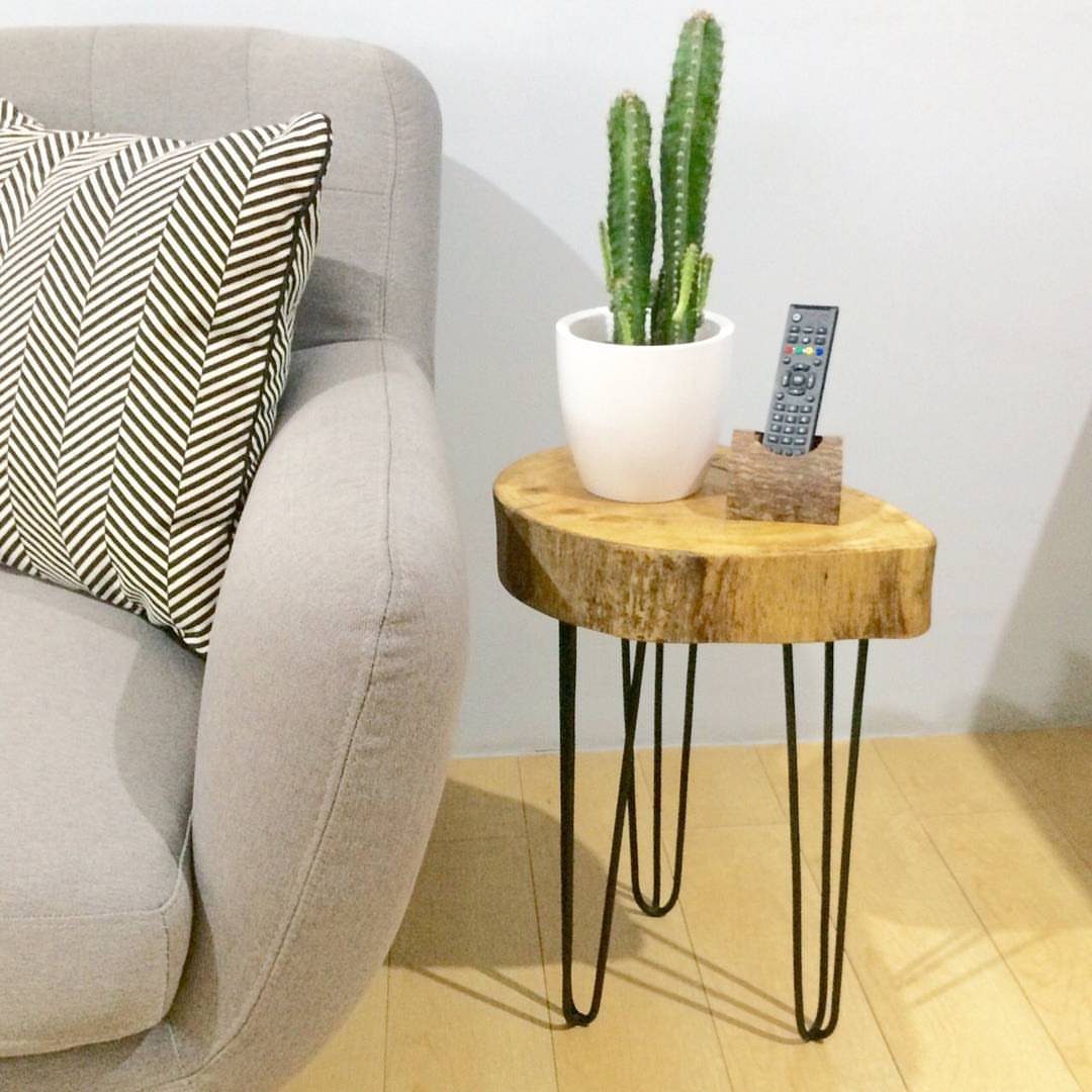 Round wood slab side table with black metal hairpin legs and a cactus.