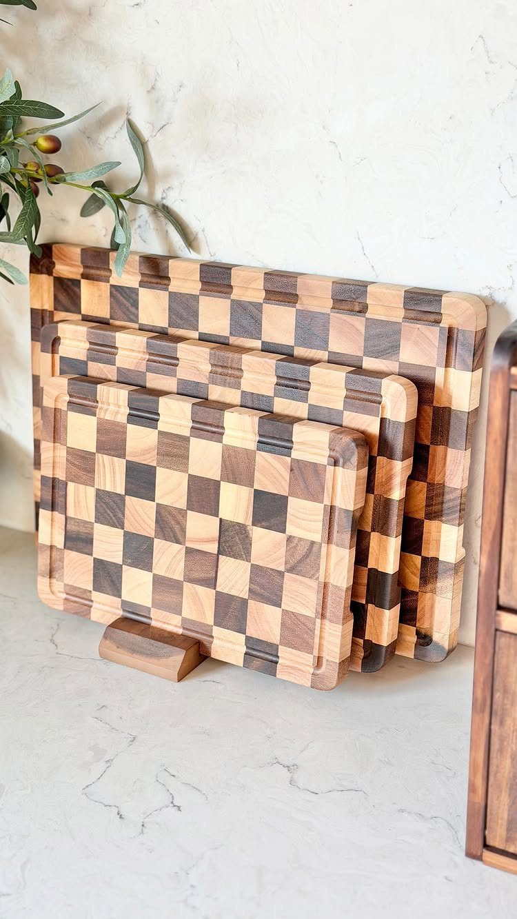 17 Wood Art Projects for Beginners and Weekend Makers 11 Three checkered wooden cutting boards leaning against a white marble wall with olive leaves.