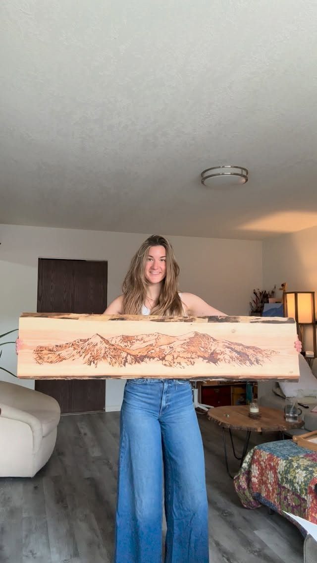 Wood Burned Pine Trees: 4 Ideas for Pyrography 3 Woman holding a long wooden plank with wood burned pine trees and mountains.
