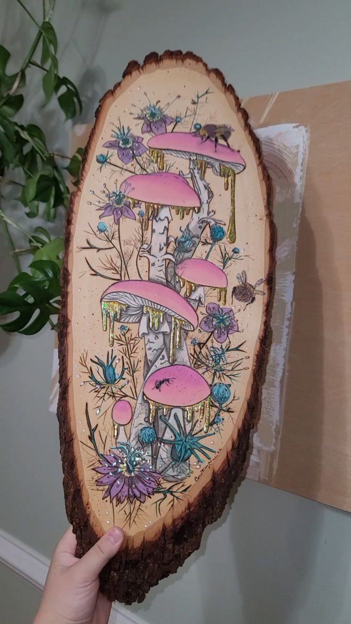 Wood burned art on a bark slice featuring pink mushrooms and purple flowers.