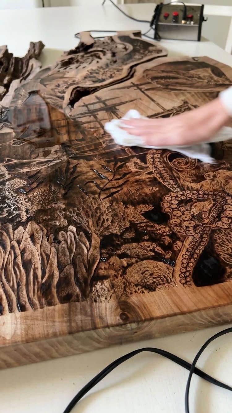 Hand applying glossy finish to a detailed wood burned art piece on wood