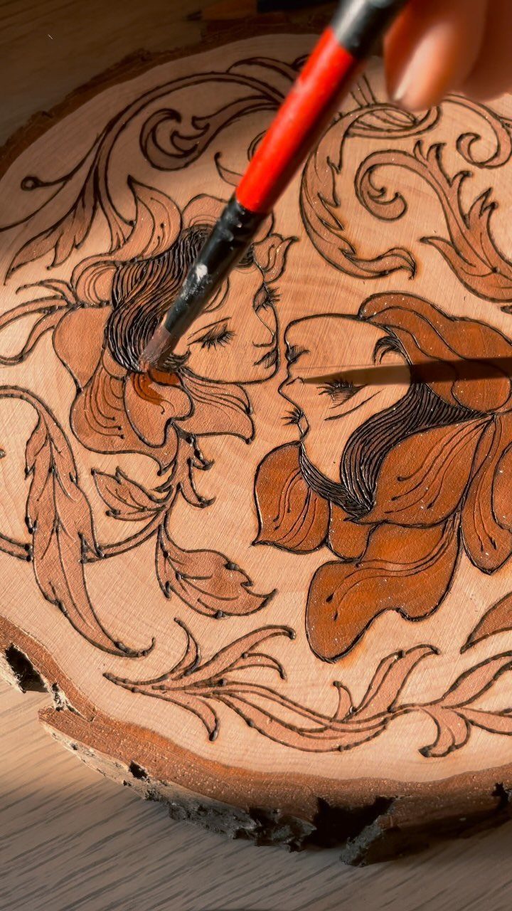 Wood burning tool creating a detailed artistic design on a natural wood slice.