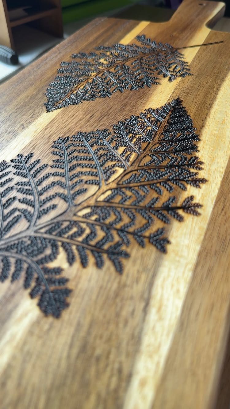 Two detailed fern leaves burned into a light-colored wooden cutting board.