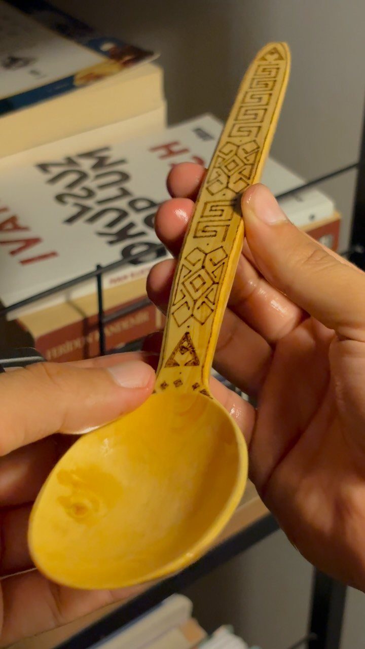 Wooden spoon with intricate geometric wood burning patterns on the handle held by hands.