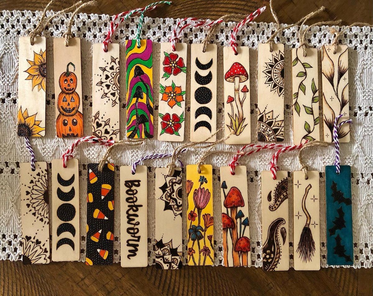 Wooden bookmarks with wood-burned designs and colorful strings on a white lace cloth.