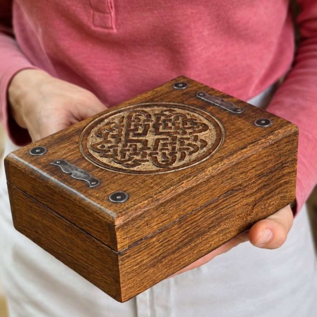 Wooden box with a carved Celtic knot design held by a person.
