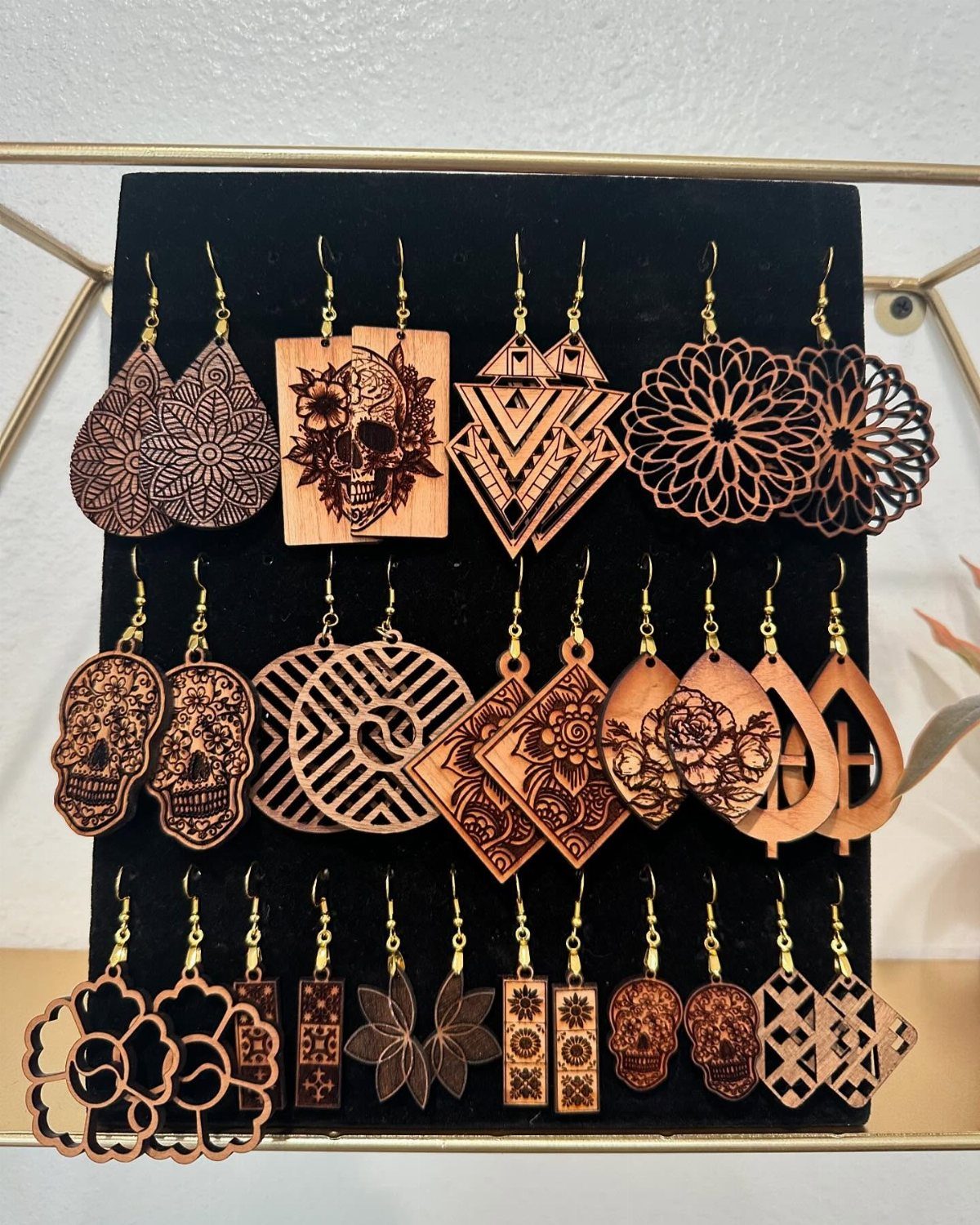 Wood-burned earrings with intricate skull and mandala designs displayed on black velvet.