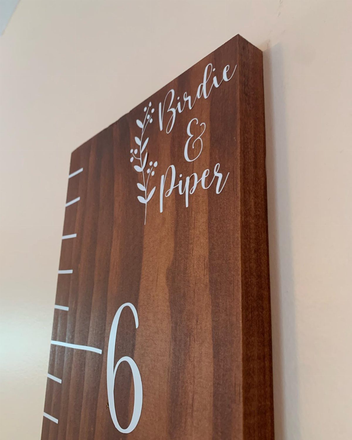 Wooden growth chart on a wall with names Birdie and Piper in white script.