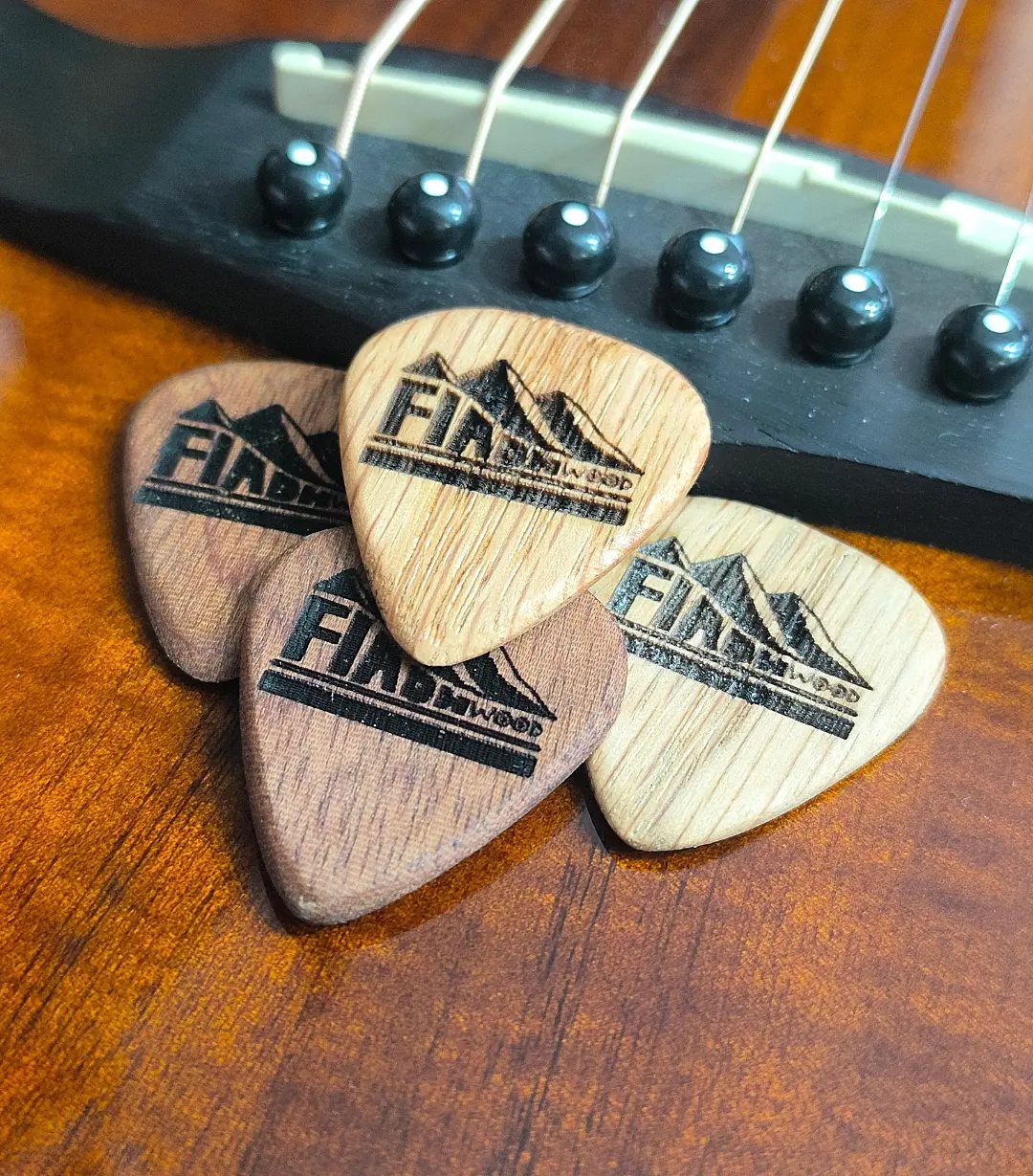 Wooden guitar picks with burned mountain logos resting on an acoustic guitar body