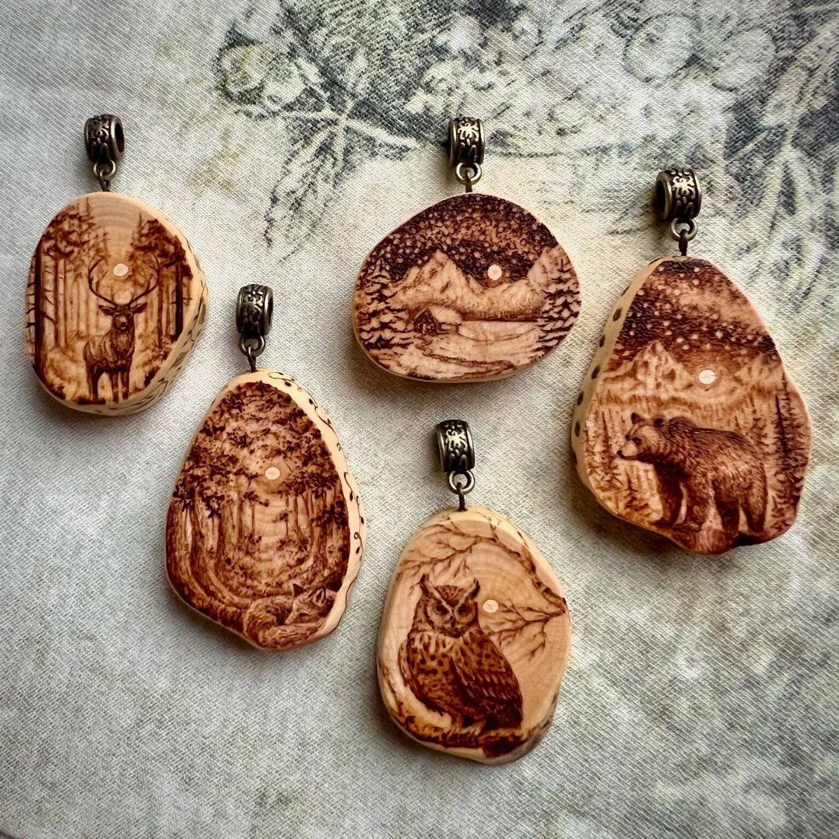 Wooden jewelry charms with detailed wood-burned images of forest animals and landscapes.