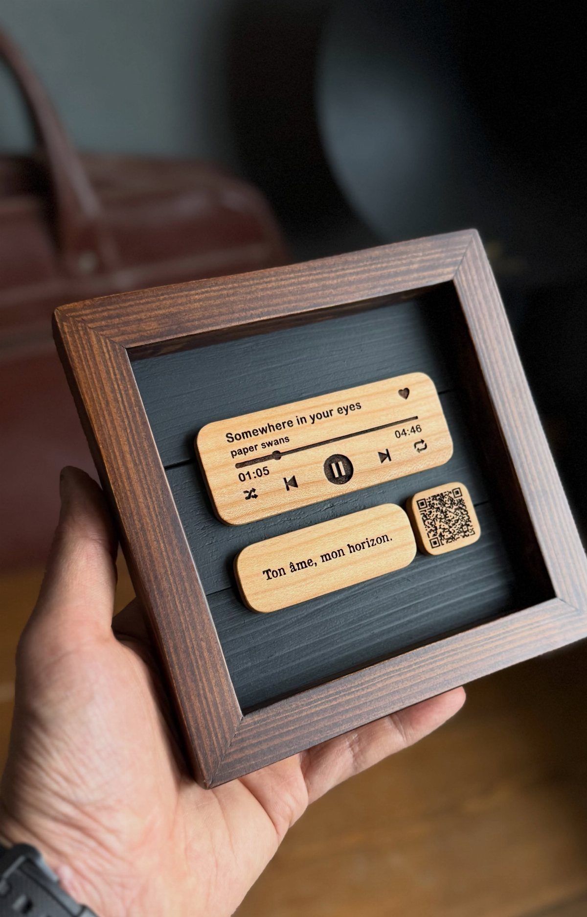 Wooden music player interface inside a dark brown frame held by a hand.