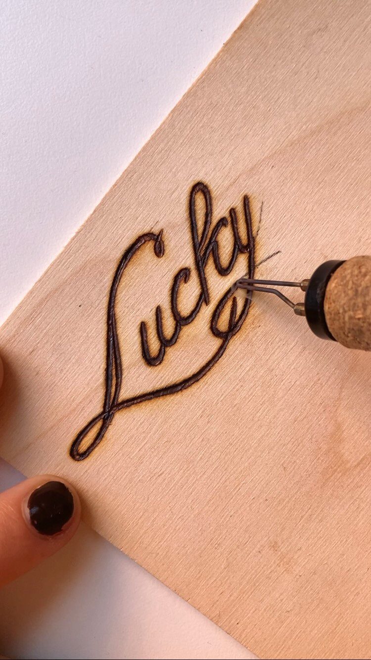 Wood Burning Lettering Ideas: 4 Styles to Try Next 3 Wood-burning tool creating the word Lucky in cursive script on a wooden board