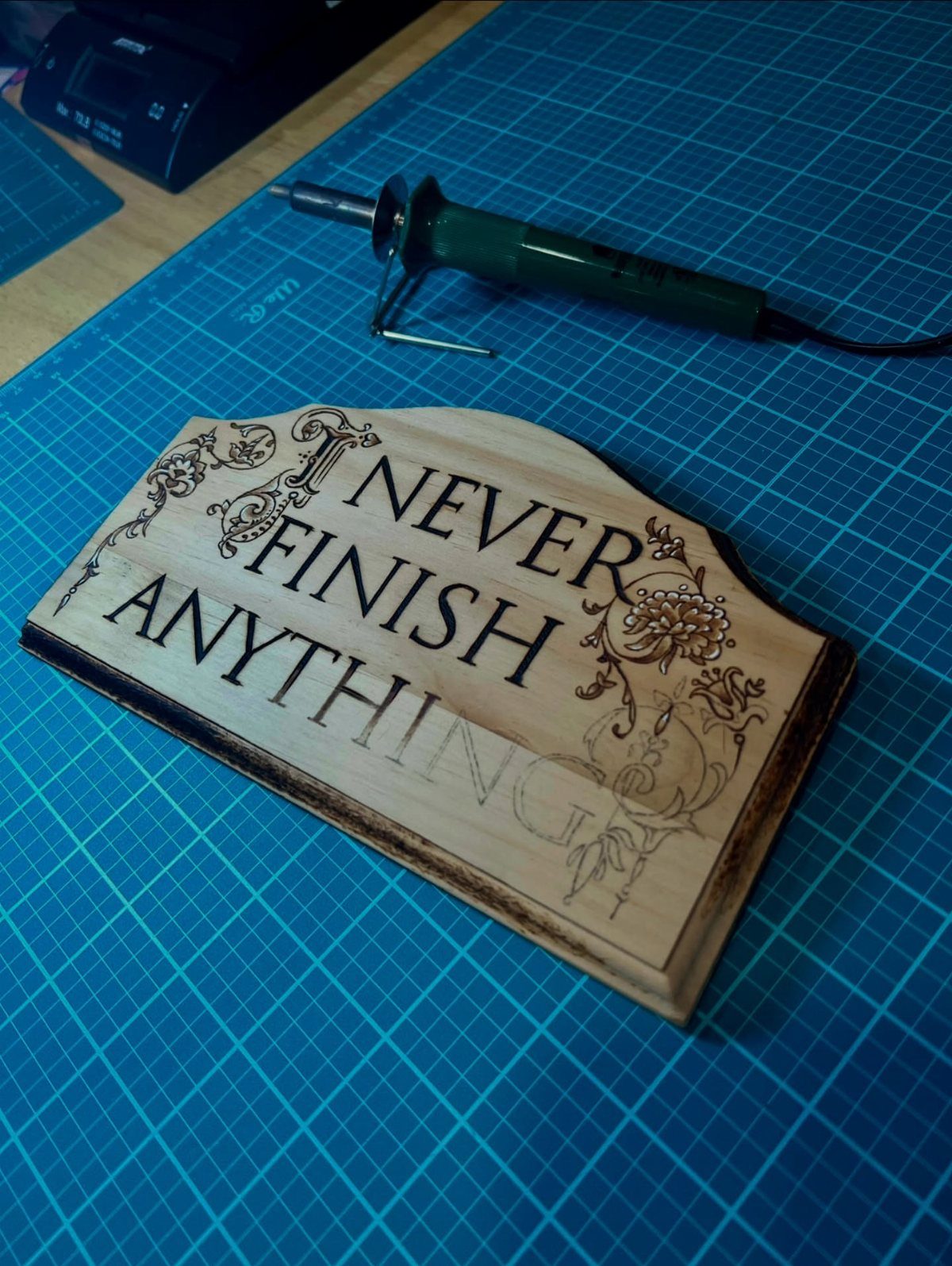 Wood Burning Lettering Ideas: 4 Styles to Try Next 1 Wooden plaque with burned lettering and floral designs next to a wood-burning tool.