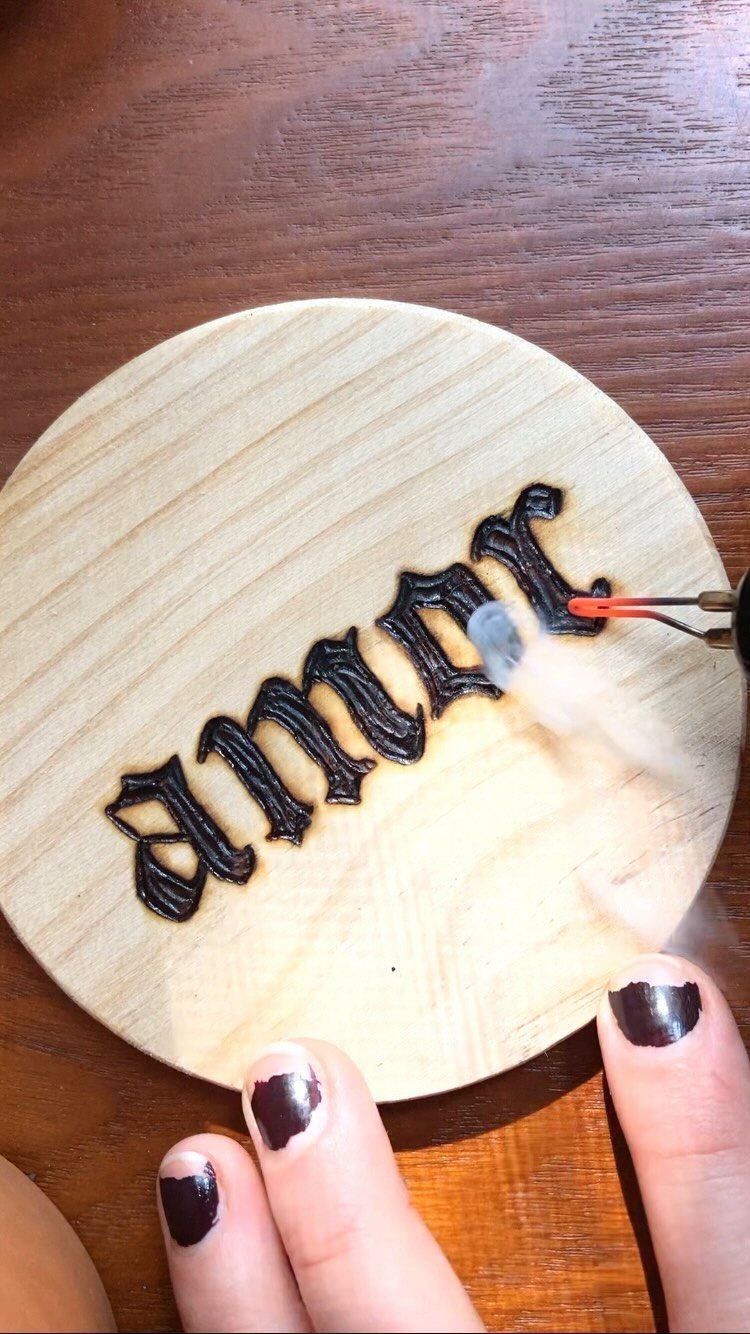 Wood Burning Lettering Ideas: 4 Styles to Try Next 2 Wood-burning tool creating gothic black lettering on a circular light wood plaque.