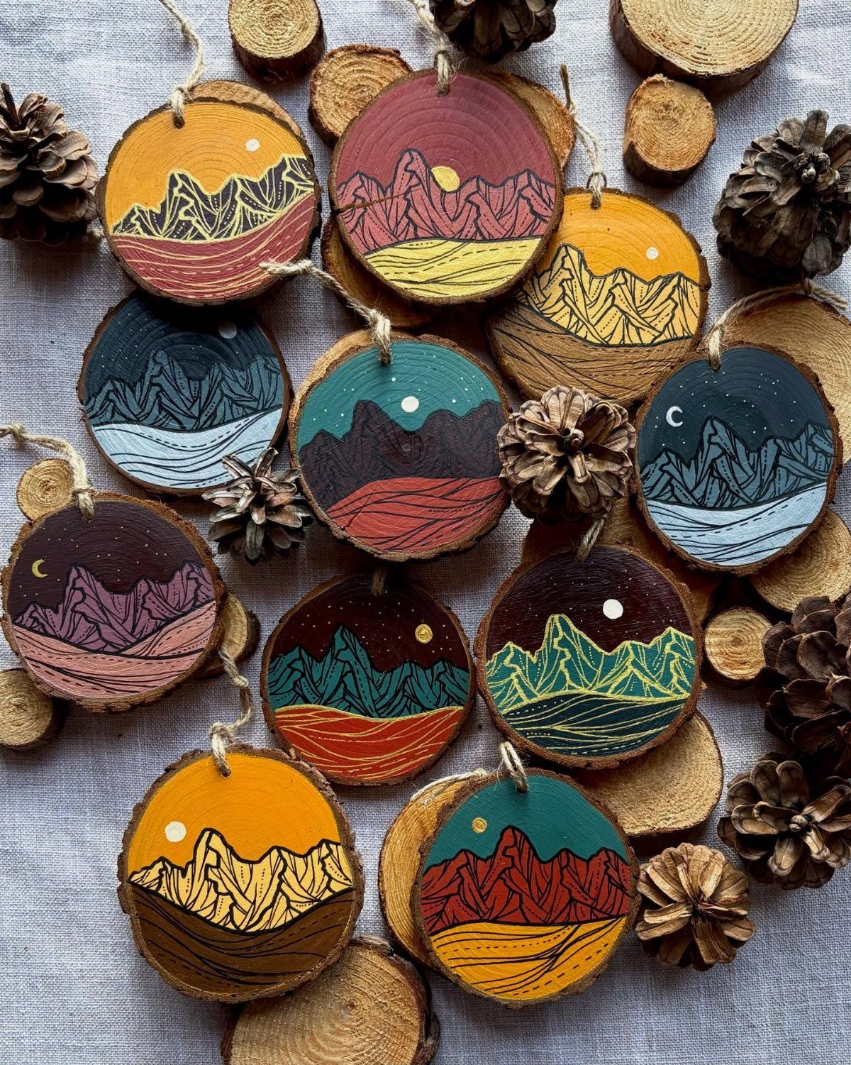 Wood Burning Ornaments: 8 Ideas for Christmas 6 Wooden slice ornaments with burned and painted mountain landscapes and pinecones on fabric
