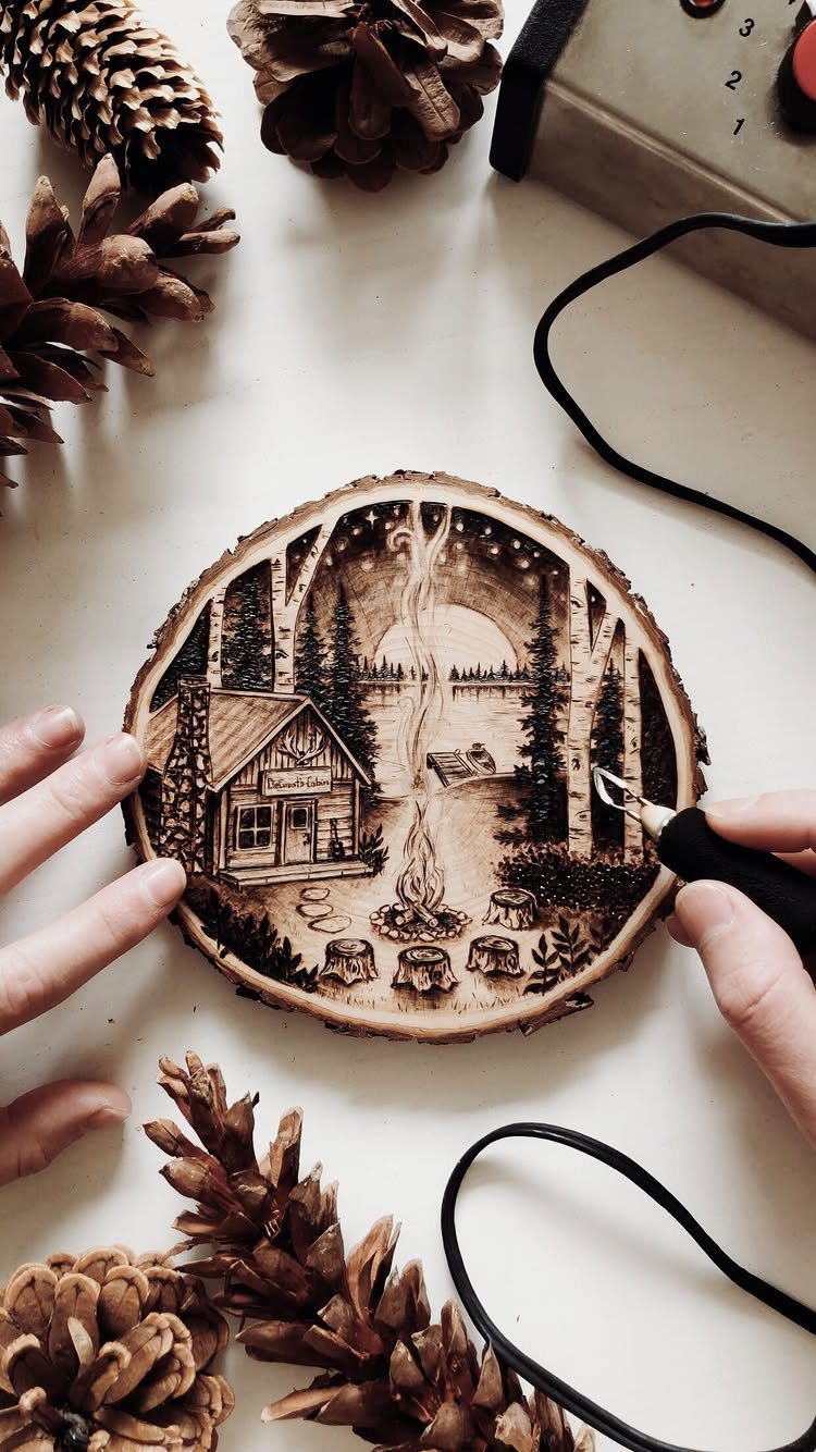 Wood-burned scene of a cabin and birch trees on a natural wood slice.