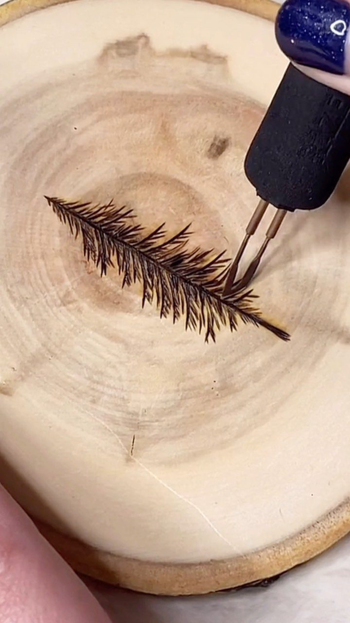 Wood burning tool creating a detailed pine needle pattern on a circular wood slice.