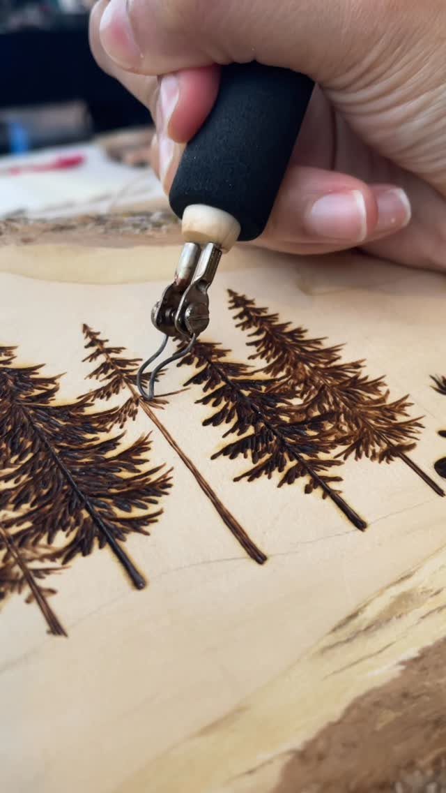 Hand using a pyrography tool to burn evergreen tree patterns into light wood.
