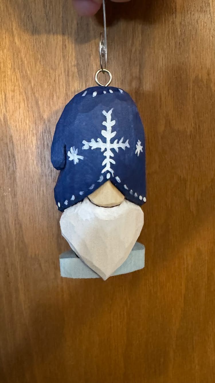 Carved wooden Christmas ornament of a bearded figure wearing a blue snowflake hat.