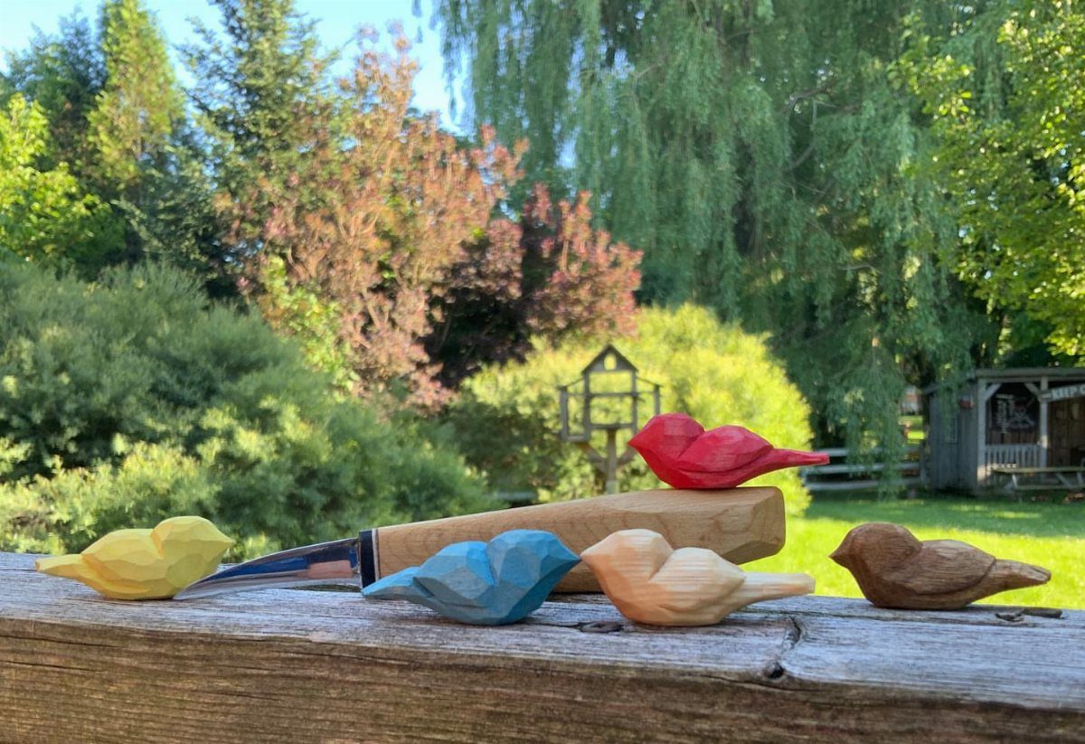 Small colorful carved wooden comfort birds resting on a rustic wooden railing outdoors.