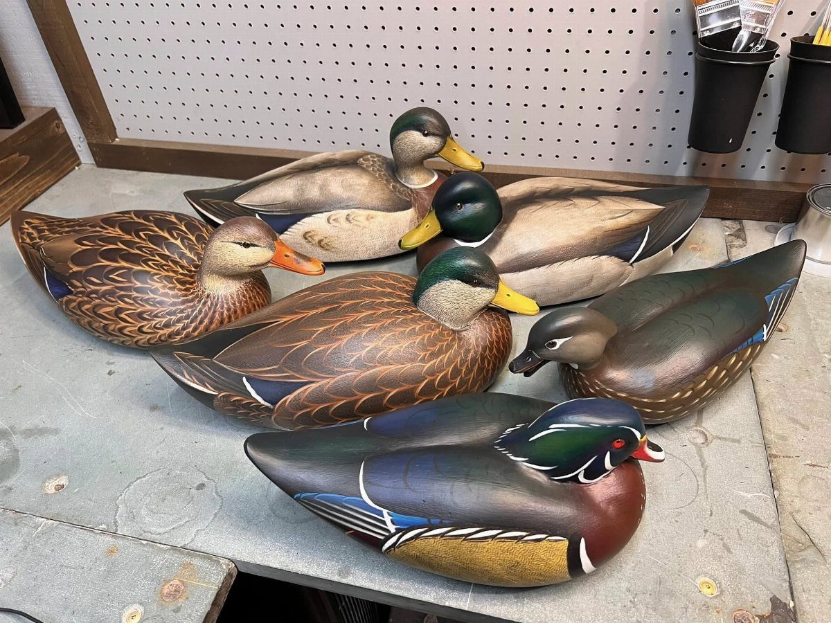 Six realistic hand-carved wooden duck decoys resting on a grey workshop workbench.
