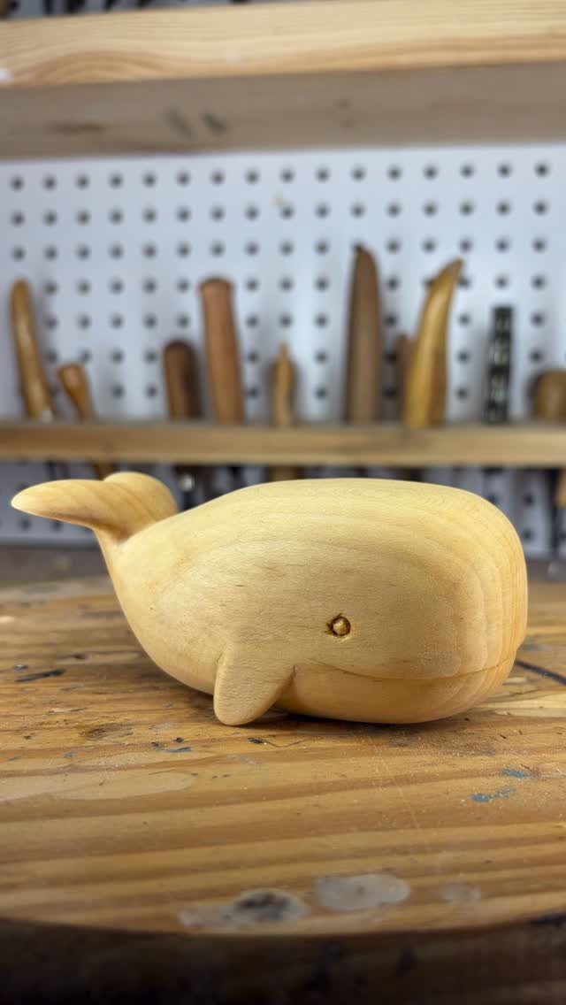 Small wooden whale carving resting on a workbench with carving tools in background