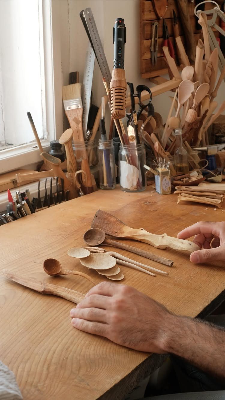 Hand-carved wooden spoons and carving tools on a wooden workbench in a workshop.