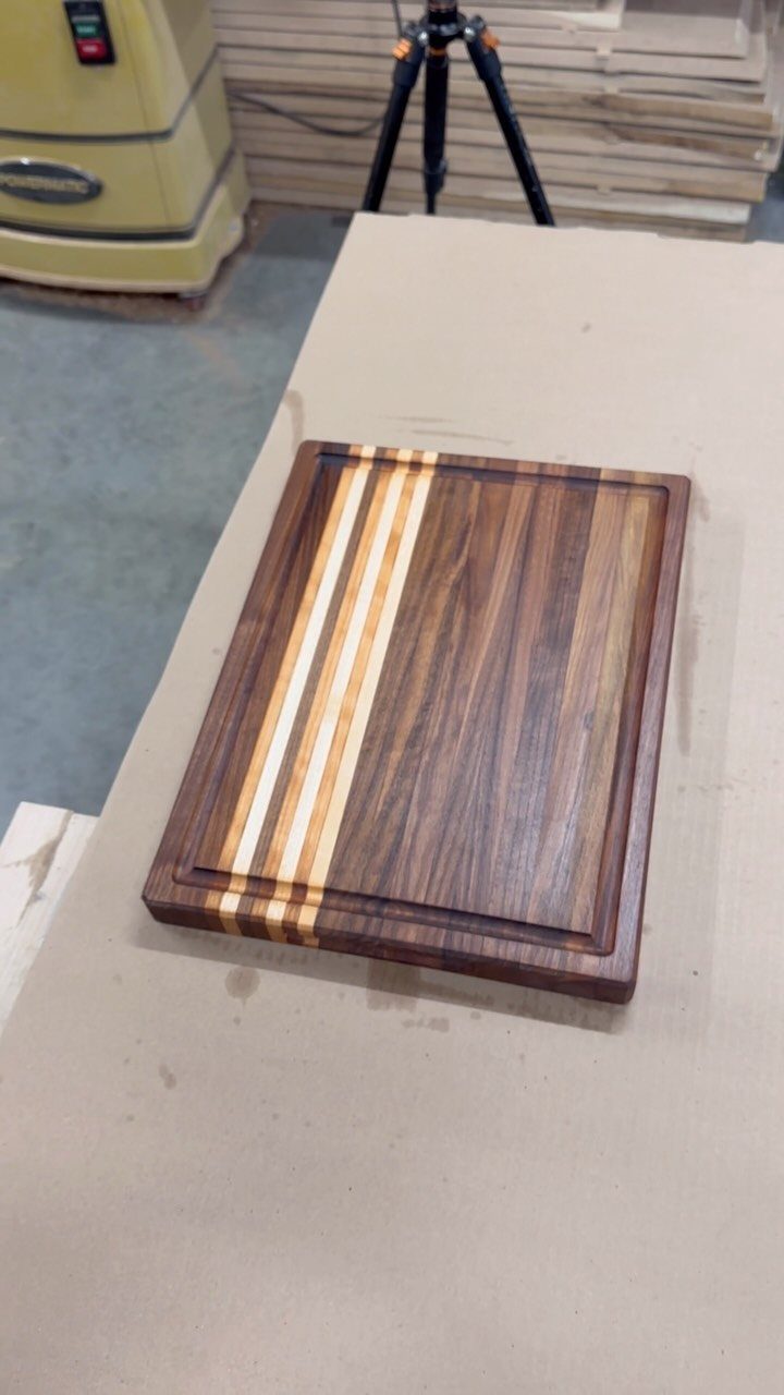 Wooden cutting board with contrasting dark and light wood strips on a workbench.