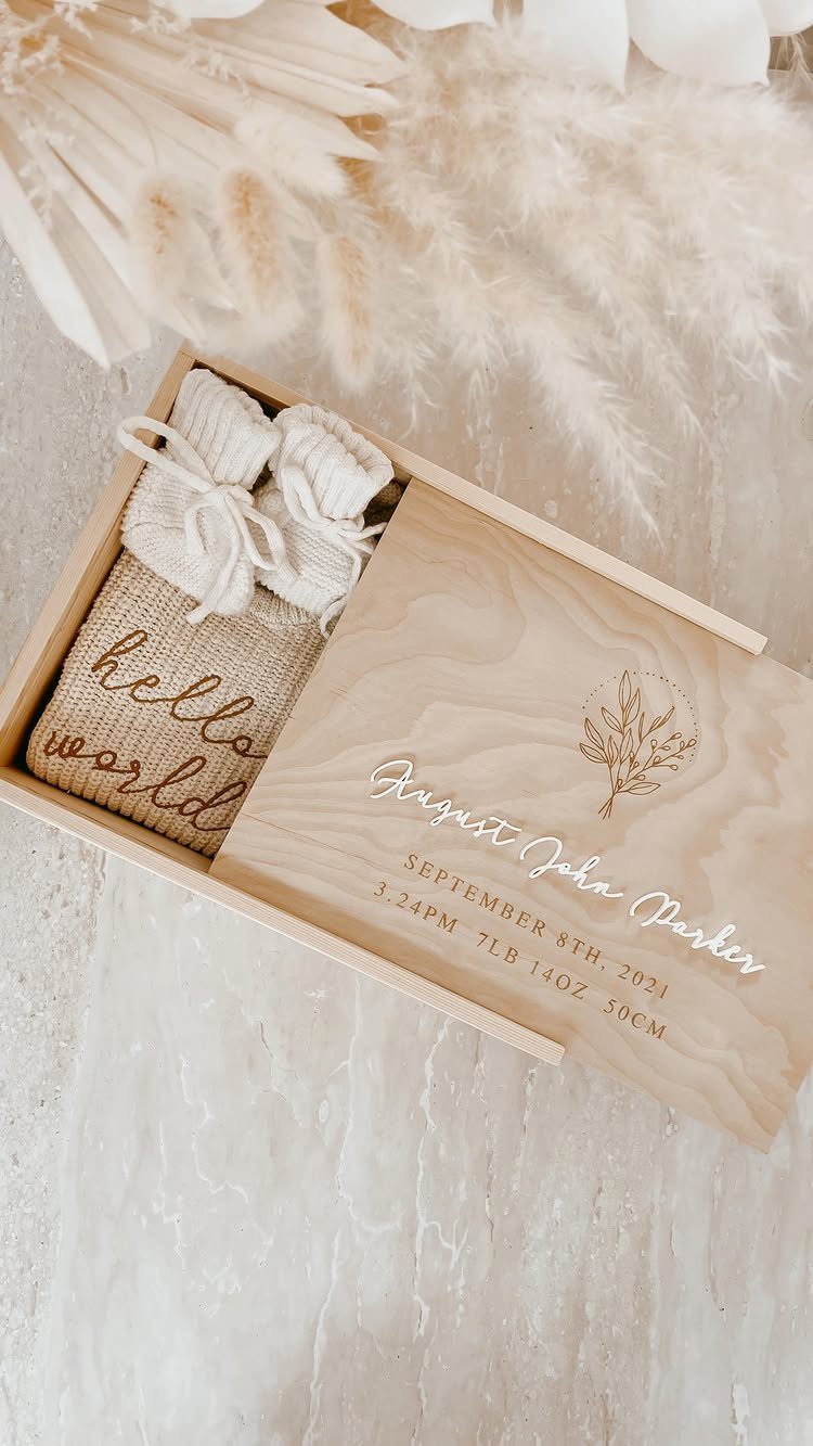 Engraved wooden memory box containing baby booties and a hello world burlap sack
