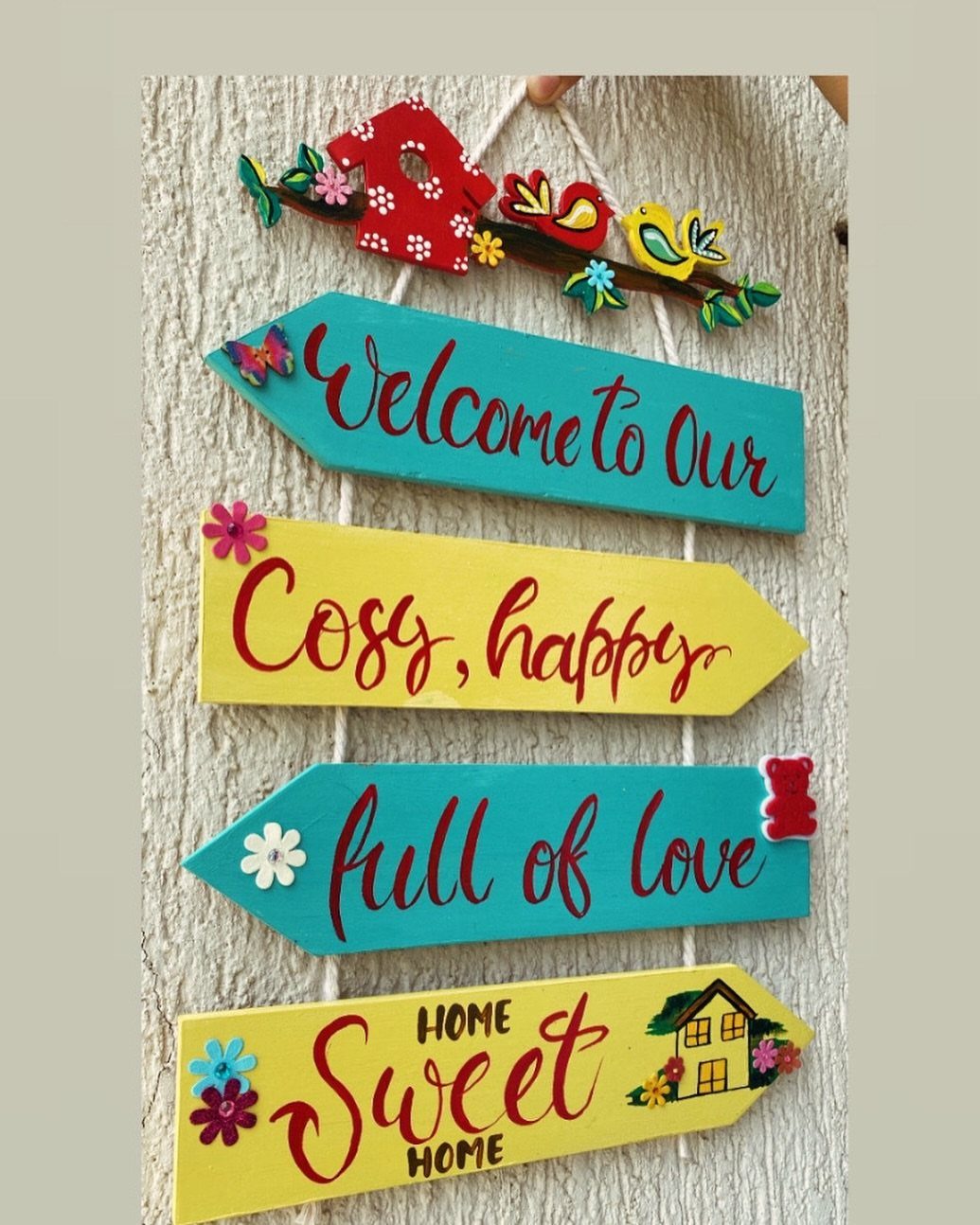 Colorful wooden arrow wall sign with cursive text and floral decorations on a white wall.