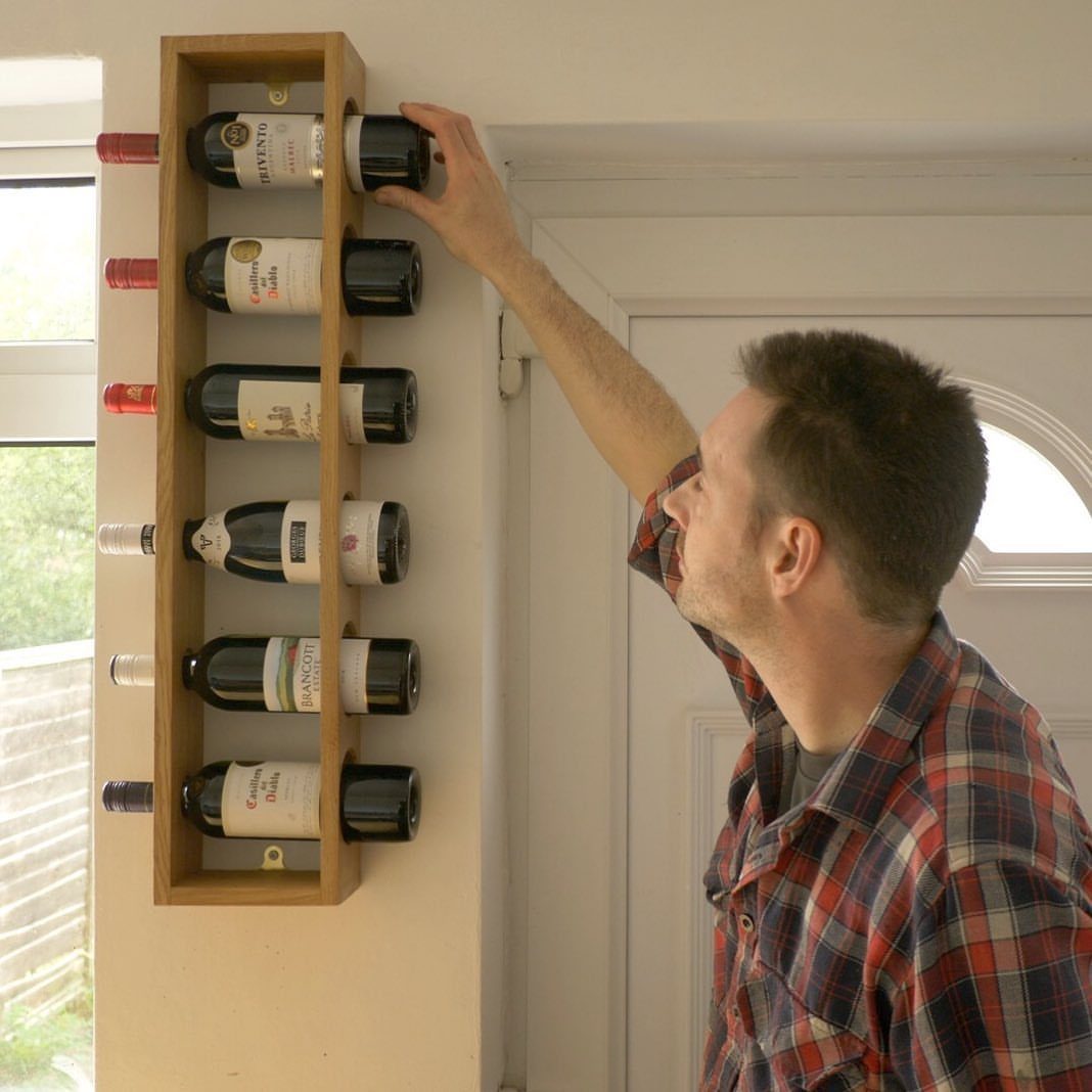 Man reaching for a bottle in a vertical wooden wall-mounted wine rack.