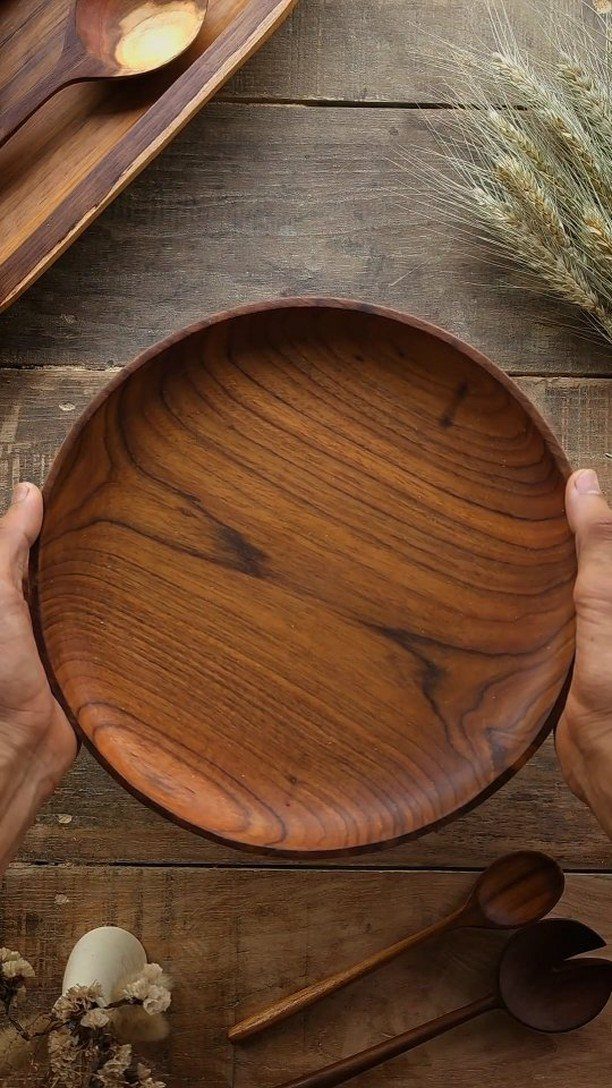 Round polished wooden serving bowl held by hands over a rustic wooden table.