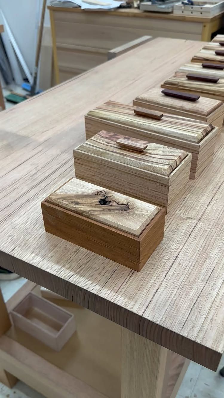 Small handcrafted wooden storage boxes with lids arranged on a light wood workbench.