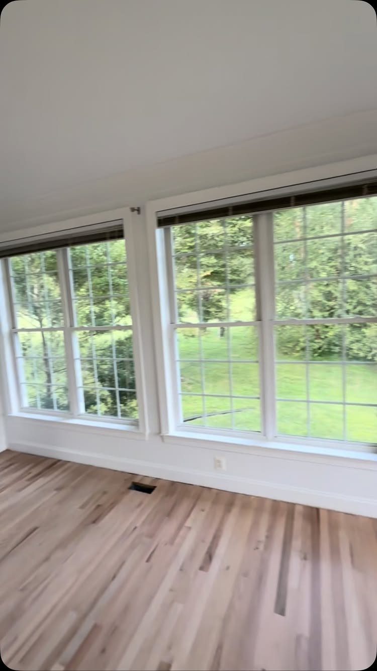 Light hardwood flooring in a bright room with two large white windows.